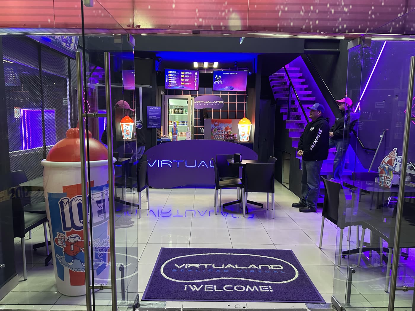 Entrada de Virtualand con tapete de bienvenida, mesas y mostrador iluminado en morado